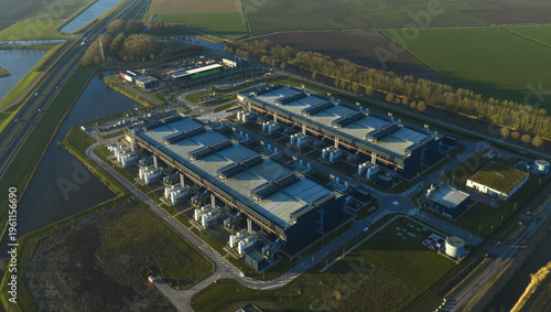 Aerial view of industrial buildings standing in stark contrast against the patchwork of green and gold fields, a modern marvel amidst rural tranquility, Middenmeer, North Holland, Netherlands.
