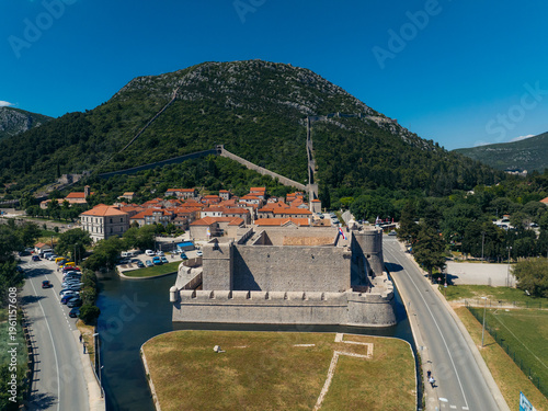 Aerial view of the imposing walls of Ston snake up the verdant hills, a testament to history against the bright Croatian sky, Ston, Dubrovnik-Neretva County, Croatia.