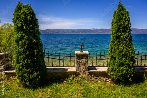 Quadro su tela A serene lakeside scene with two prominent cypress trees framing the expansive blue waters of Lake Ohrid at Holy Mother of God Zaumska Church