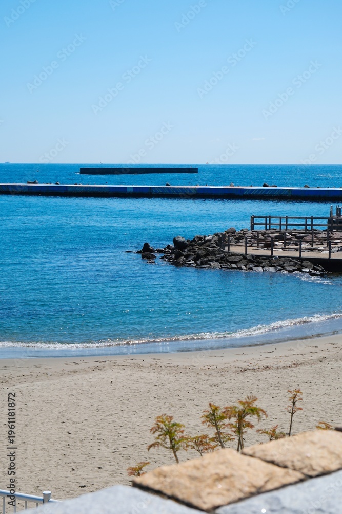 Fototapeta premium Serene sandy beach with blue ocean and distant pier on a sunny day.