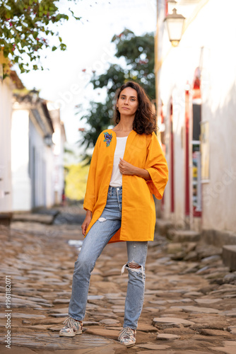 Woman stands on a cobblestone street wearing a bright outfit in a small town during a sunny day while trees and buildings frame the background