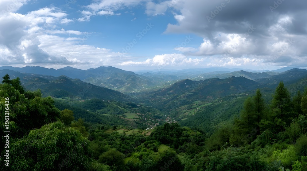Fototapeta premium Panoramic vista of a lush green valley nestled between rolling mountains under a dramatic sky with scattered clouds