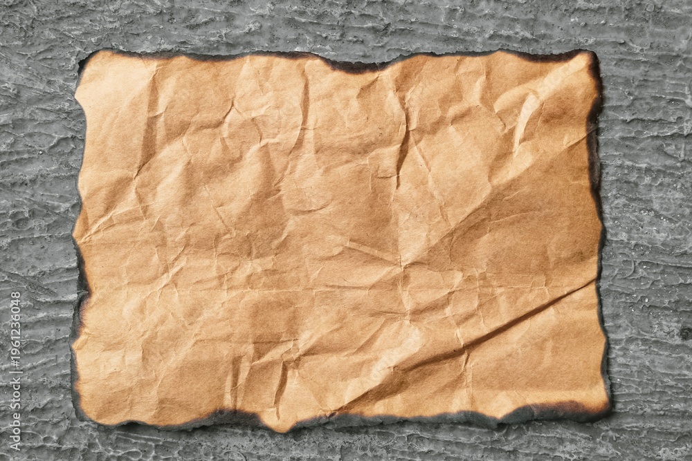 Fototapeta premium A burnt, crumpled piece of brown paper on a dark, textured background