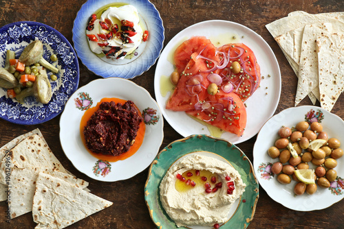 Assorted traditional Turkish mezes and appetizers on a table.

 A vibrant overhead shot of various cold appetizers on a dining table, including walnut dip (muhammara), fresh green peppers,