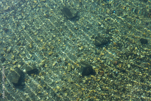 Der Grund eines klaren Sees bei gebrochenem Sonnenlicht