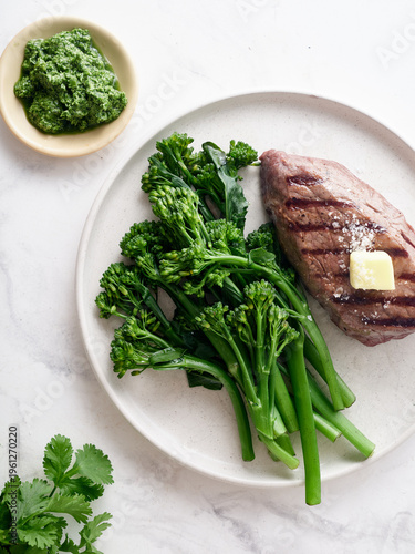 Grilled roast beef flank and rump steak served with broccolini and herb sauce on a white plate