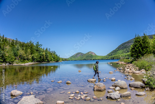 Cuadro en lienzo Lone hiker walks carefully over wet stones near a calm lake
