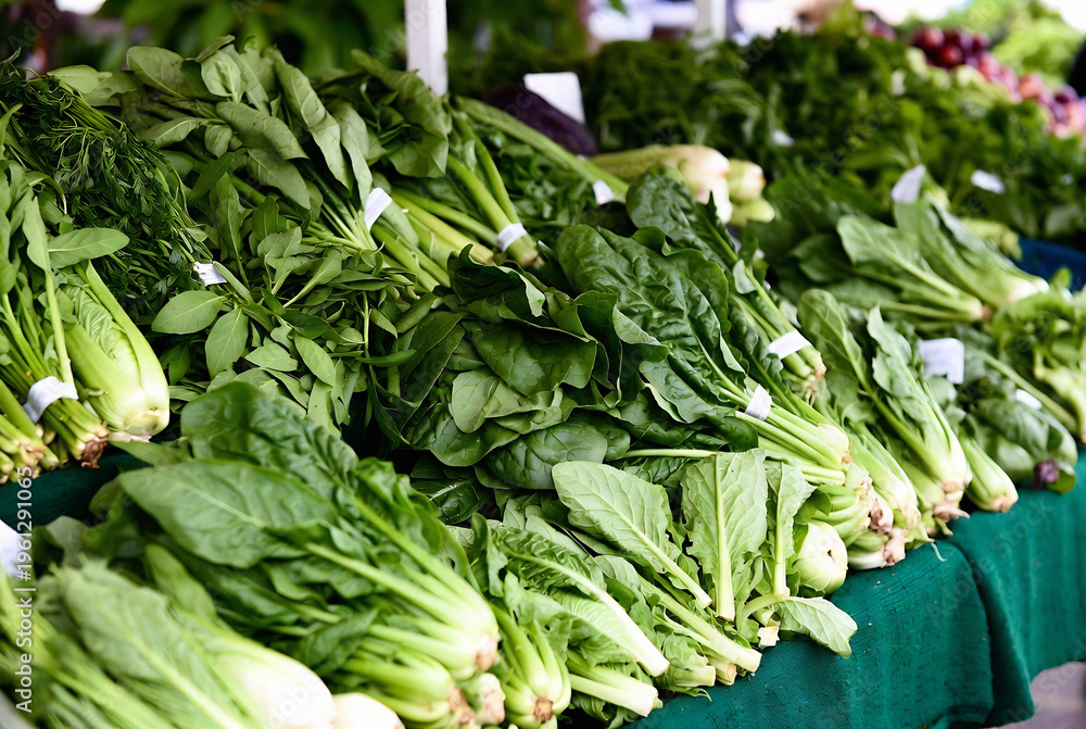 Fototapeta premium A display of fresh spinach and collard greens is at a farmer’s market. People are selling produce; the setting is an outdoor market.