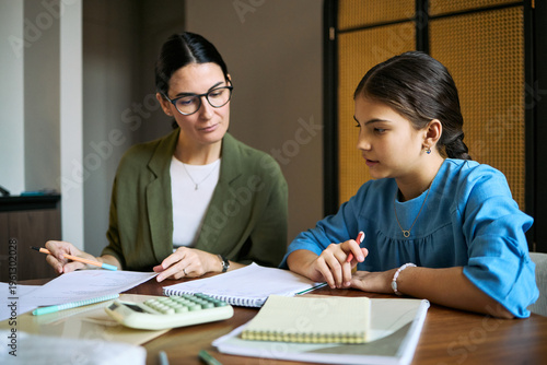 Photos Middle aged woman tutoring schoolgirl, reviewing homework and explaining math at desk