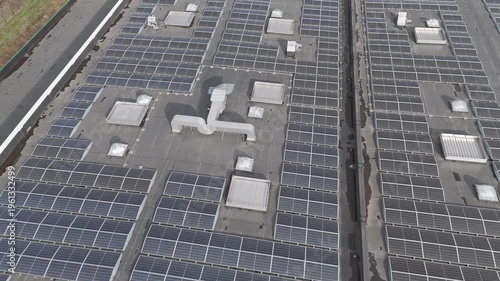 Genk, Belgium. Smooth lateral drone movement over industrial rooftop solar panels with repeating grid patterns. Backward drone flight.
