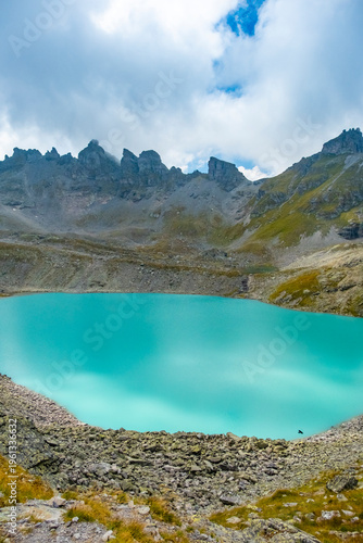 Captivating landscape of Pizol Wildsee lake in the Swiss Alps, featuring tranquil turquoise water amid rugged peaks enveloped by mist and clouds, creating a dramatic mountain scene