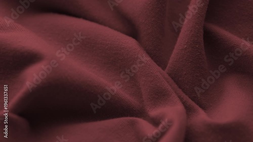 A close-up of soft burgundy red jersey fabric with elegant wavy folds and a fine knitted texture.