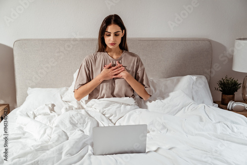 Young woman using laptop in bed for online wellness class practicing mindfulness and morning routine