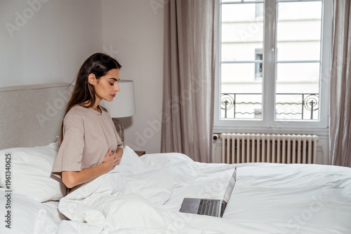 Young woman using laptop in bed for online wellness class practicing meditation and morning routine