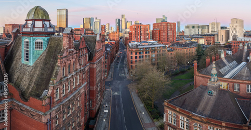 A wide aerial panorama of Whitworth St in Manchester at dawn, showing the majestic terracotta architecture leading toward the modern city skyline.