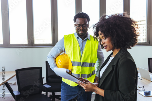 Business Meeting Between Engineer and Project Manager in Office With Hard Hat and Plans