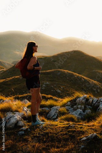 Foto Young woman standing on a mountain peak at sunset, arms open or enjoying the view, embracing nature and freedom in the mountains in Durmitor National Park, Montenegro