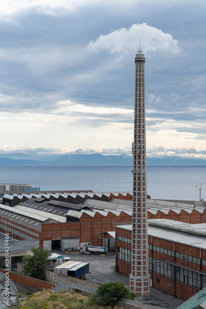 Fototapeta premium Coastal view with a tall industrial brick chimney, factory buildings. Savona, Italy