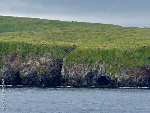 Rocky cliffs jut out above the water on Kagamil Island in the Aleutian Archipelago of Alaska during a cloudy day