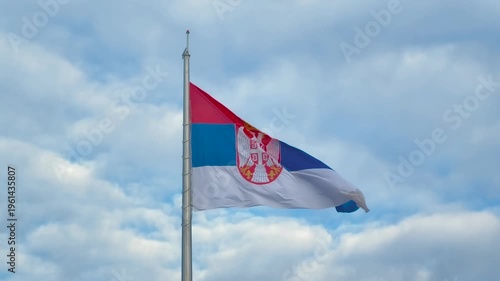 Serbian national flag waving on a flagpole in strong wind in Belgrade, Serbia - close up view. Cloudy sky in the background, outdoor daytime scene