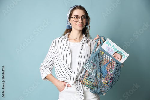 Woman holding net bag with magazines on light blue background