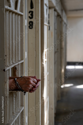 Closeup of hands with hand cuffs resting on cell door in prison.