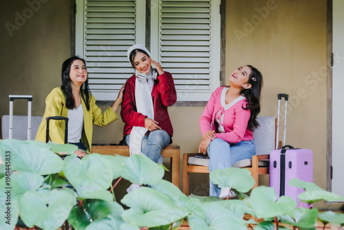 Three radiant young women, suitcases at their sides, share a joyful moment of laughter before embarking on their travel. Capturing the essence of friendship and exciting adventure.