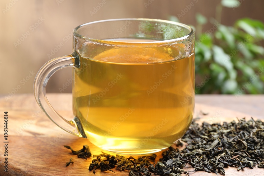 Fototapeta premium Refreshing green tea and dry leaves on wooden table, closeup