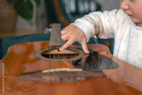 Little child playing acoustic guitar strings close up. Child exploring guitar.