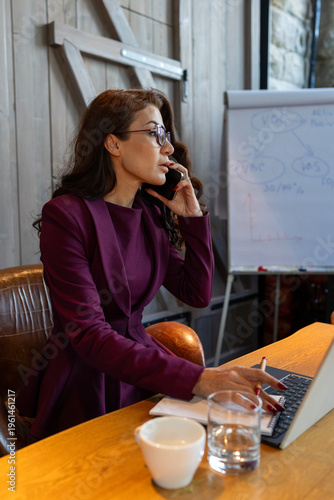 Fashion creator reviews design samples and schedules in studio environment. Stylish female designer discusses production details and timelines in vibrant workspace environment