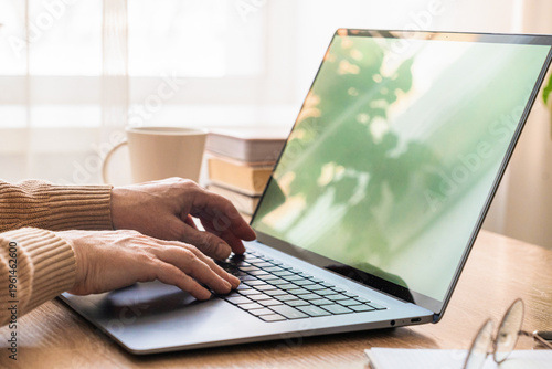 Womens hands typing on laptop keyboard, working remotely from home office desk with mug and glasses. Person typing on laptop working from home