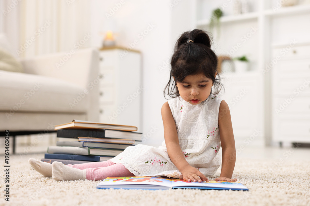 Obraz premium Cute little girl reading book on floor at home. Space for text