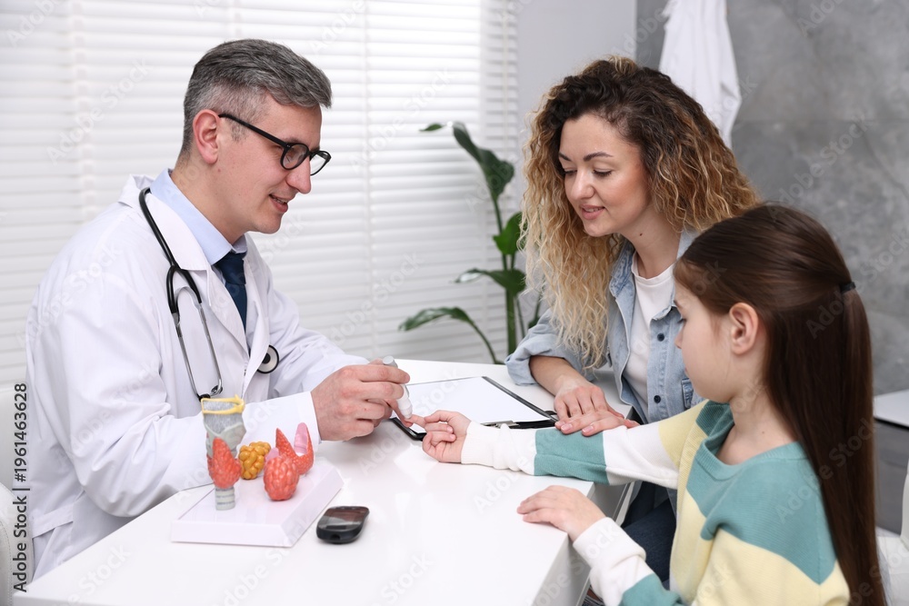 Obraz premium Endocrinologist in glasses checking little girl's blood sugar level with lancet pen while her mother supporting her at white desk in clinic