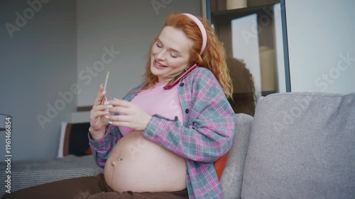 Pregnant woman sitting on couch files his nails with a nail file while talking on phone in a modern living room during daylight