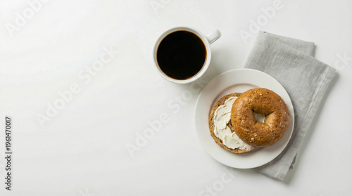 Toasted bagel with cream cheese and black coffee cup on white surface with copy space