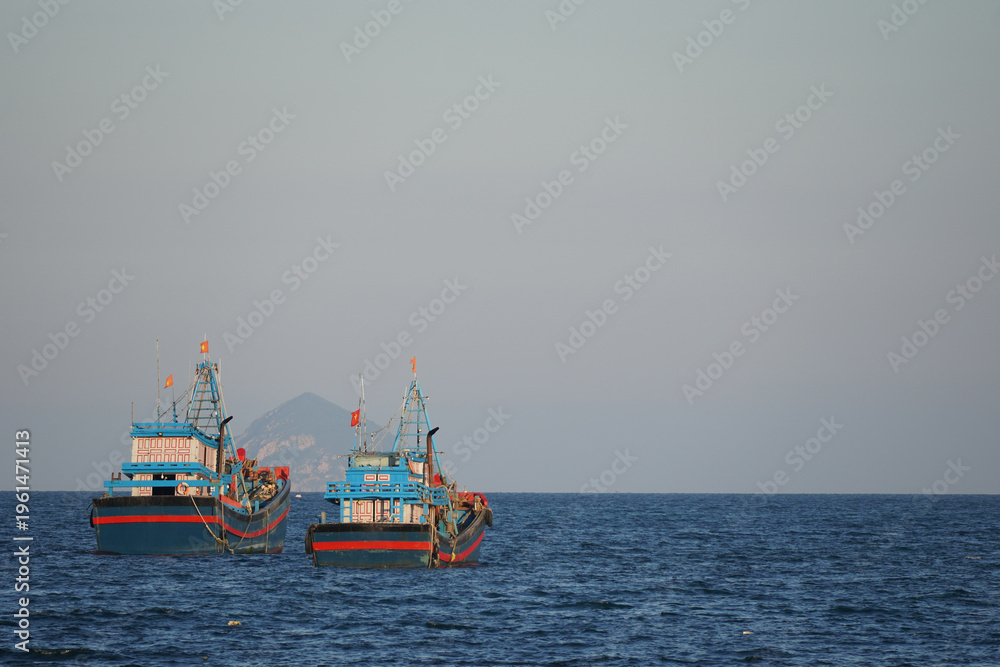 Fototapeta premium Traditional blue and red wooden fishing vessels at sea with a mountain silhouette in the background