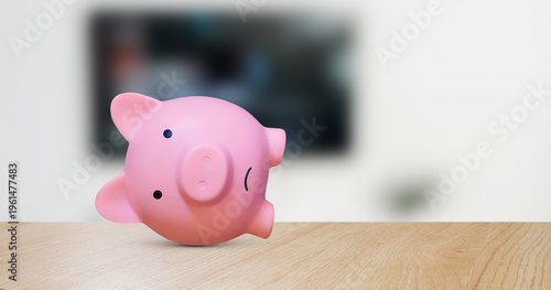 Depressed pink piggy bank lying on its side without money on a wooden surface