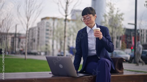 Businesswoman in blue suit working on laptop and drinking coffee outdoors