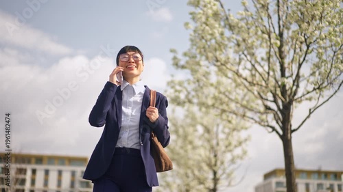 Young businesswoman in glasses talking on phone while walking in a city park