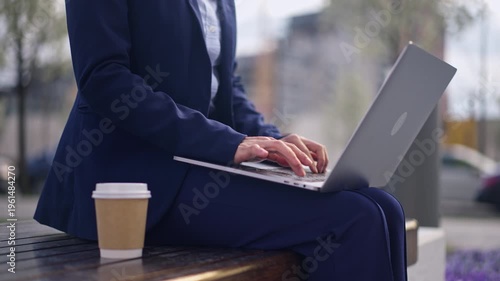 Businesswoman working on laptop outdoors with coffee, focused on tasks