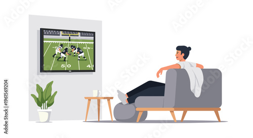 A man with a top bun relaxes on a grey armchair with his feet up, watching American football on a wall-mounted television.