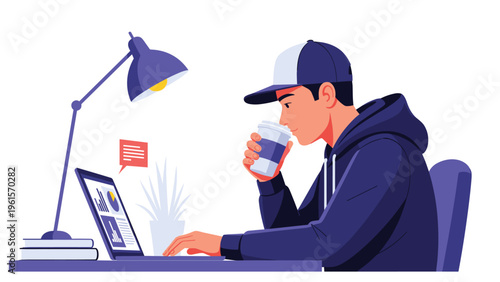 Young man wearing a hoodie and cap working on a laptop while drinking coffee at a dark workspace lit by a desk lamp.