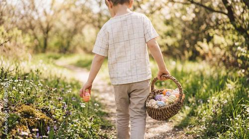 Young boy seen from behind, walking on a sunlit path through lush spring greenery.