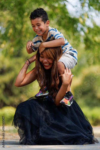 Fotografie Playful moment between a smiling young boy sitting on a woman's shoulders outdoo