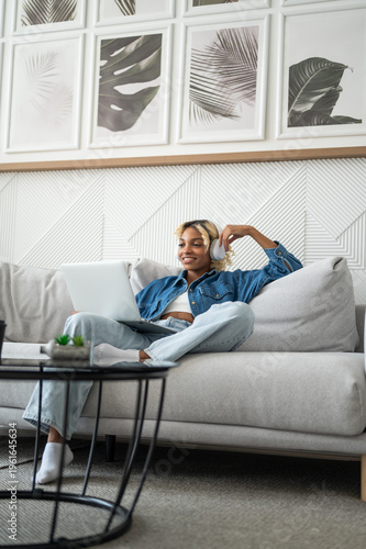 Vertical banner with Smiling young black girl in headphones watching movie or film on streaming service on her laptop.