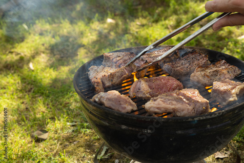Grilling Meat Over Open Flame in a Backyard on a Sunny Day With Friends Nearby