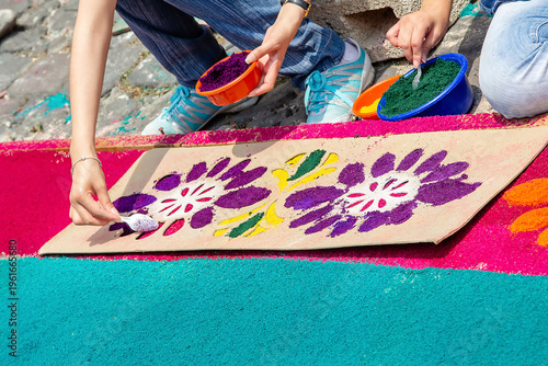 Slika na platnu Hands creating colorful sawdust carpet using stencil on street in Antigua Guatem