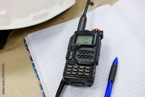 Construction Site Communication: Walkie-Talkie, Notebook and Hard Hat Close-up