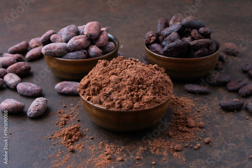 Cocoa beans and a pile of cocoa powder in wooden bowls on a stone table