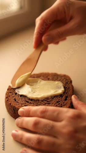 Spreading butter on rustic rye bread slice with natural morning light